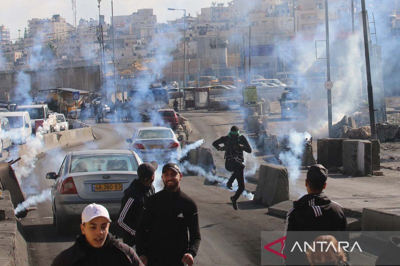 Para warga Palestina pengunjuk rasa berlarian untuk berlindung dari tabung gas air mata yang ditembakkan oleh pasukan keamanan Israel dalam bentrokan di pos pemeriksaan Qalandia dekat Kota Ramallah di Tepi Barat (27/12/2022). ANTARA
