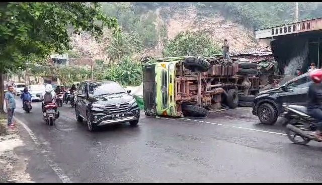 Diduga tak kuat menanjak, mobil truk bermuatan bahan-bahan pokok terguling dan menabrak satu rumah warga di Jalan Singsingamangaraja, Gedung Air, Bandar Lampung, pada Kamis (22/6/2023).